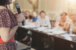 Woman with microphone speaks to the public.
